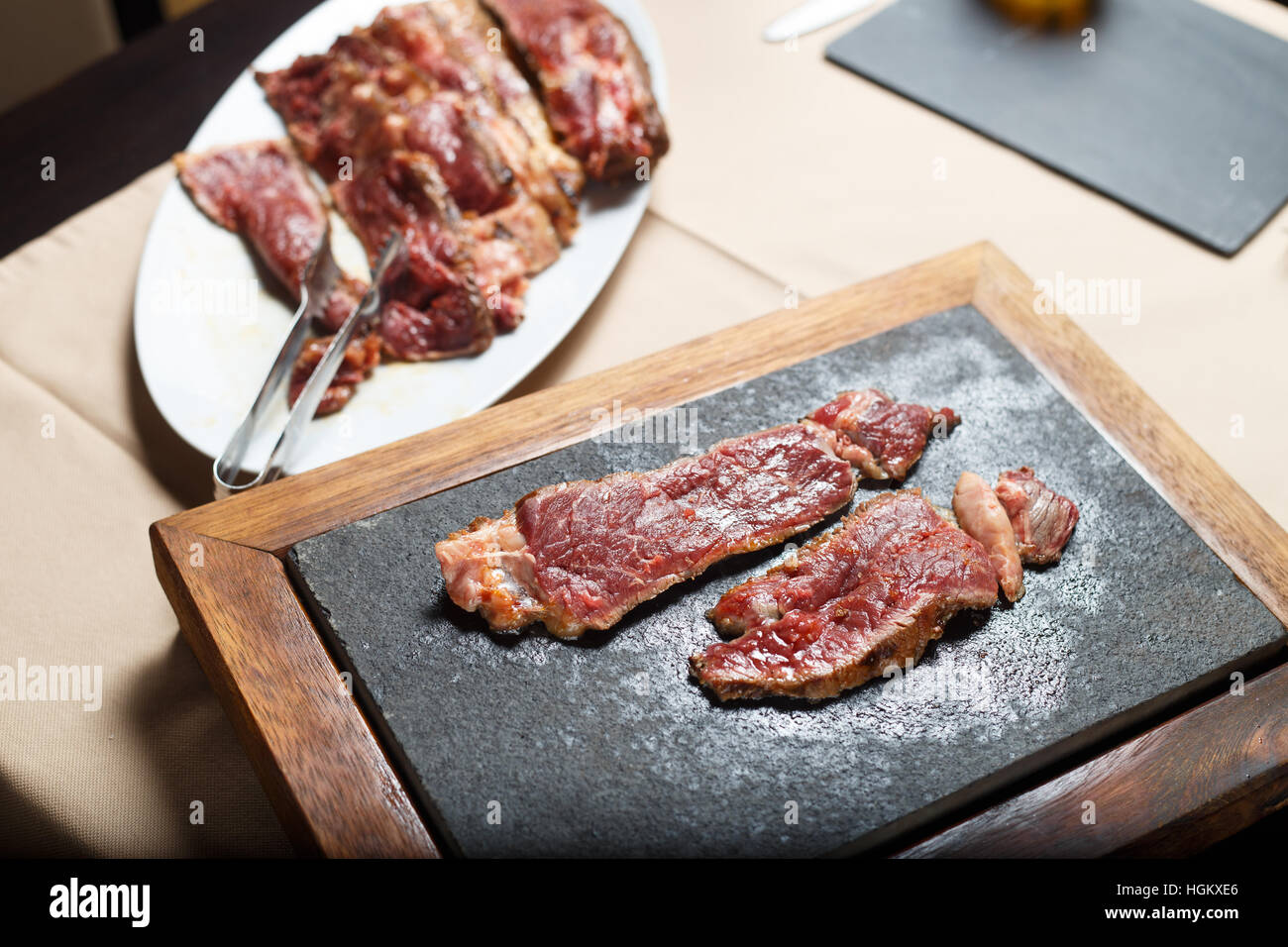 Corte el bistec de carne en una placa blanca y placa caliente shot con luz artificial. Foto de stock