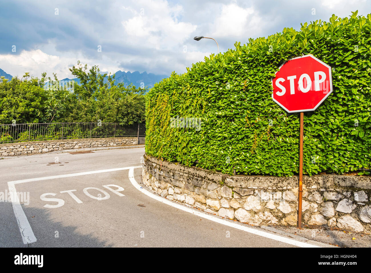 Cruce con símbolo de stop pintado sobre el asfalto y hexagonal rojo señal de pare en poste de metal. Junto a los caminos rurales de la ciudad de Como, Italia Foto de stock