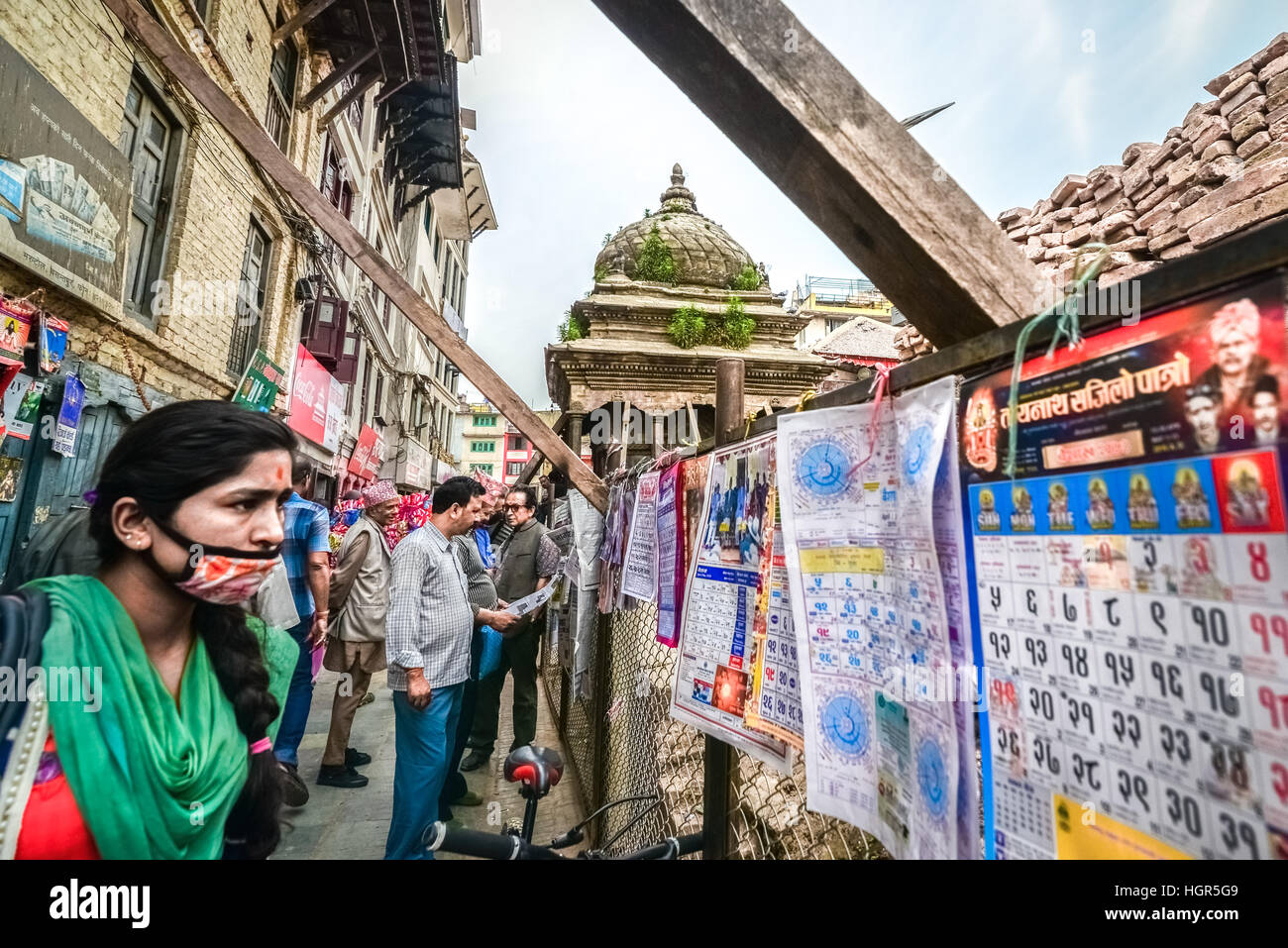Una mujer lleva una máscara de polvo mientras presta atención a los calendarios que se venden en una tienda callejera en Katmandú, Nepal. Foto de stock