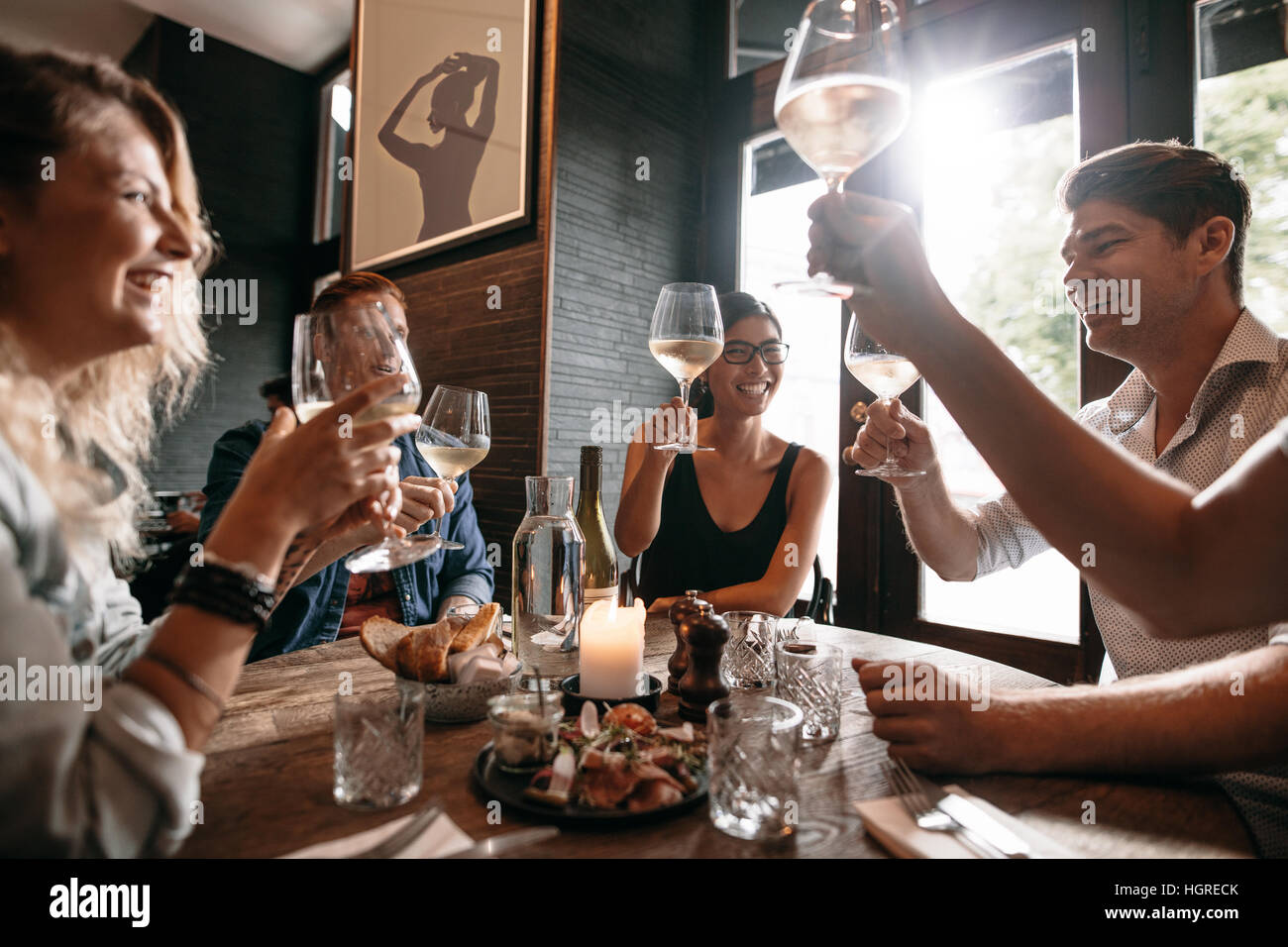 Un grupo de amigos, hacer un brindis en el restaurante. Los jóvenes amigos sentado en una mesa, brindando con vino y disfrutar de una comida juntos. Foto de stock