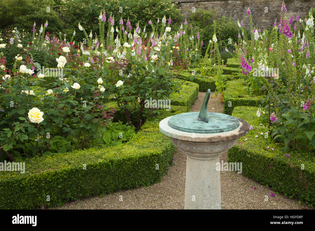 El Sundial ornamentales con foxgloves y rosas en el parterre en el jardín amurallado de Rousham Casa en Oxfordshire, Inglaterra Foto de stock
