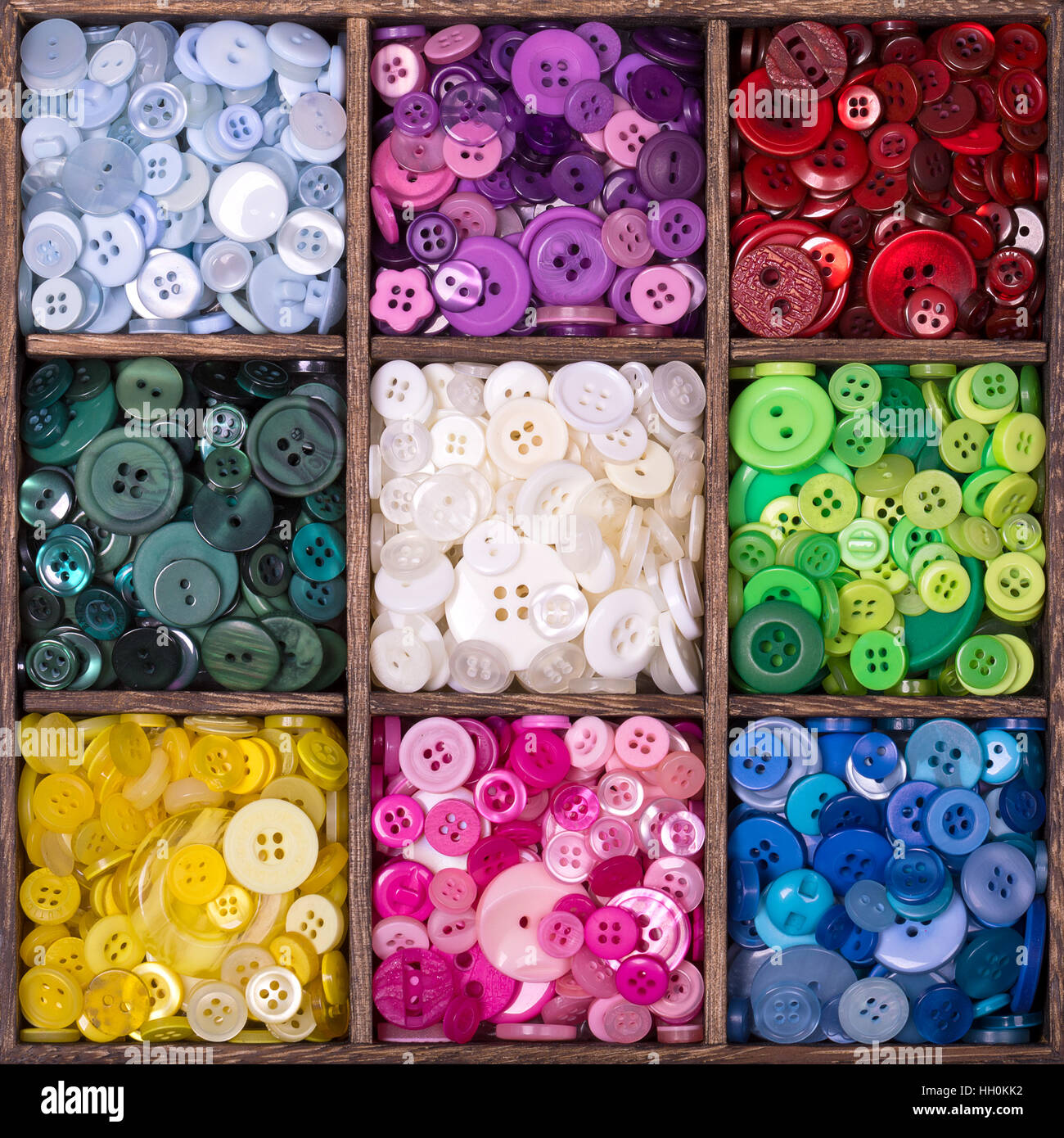 Caja de almacenamiento de madera cuadrada con 9 compartimentos, rellenos con una selección de coloridos botones agrupados por color. Foto de stock