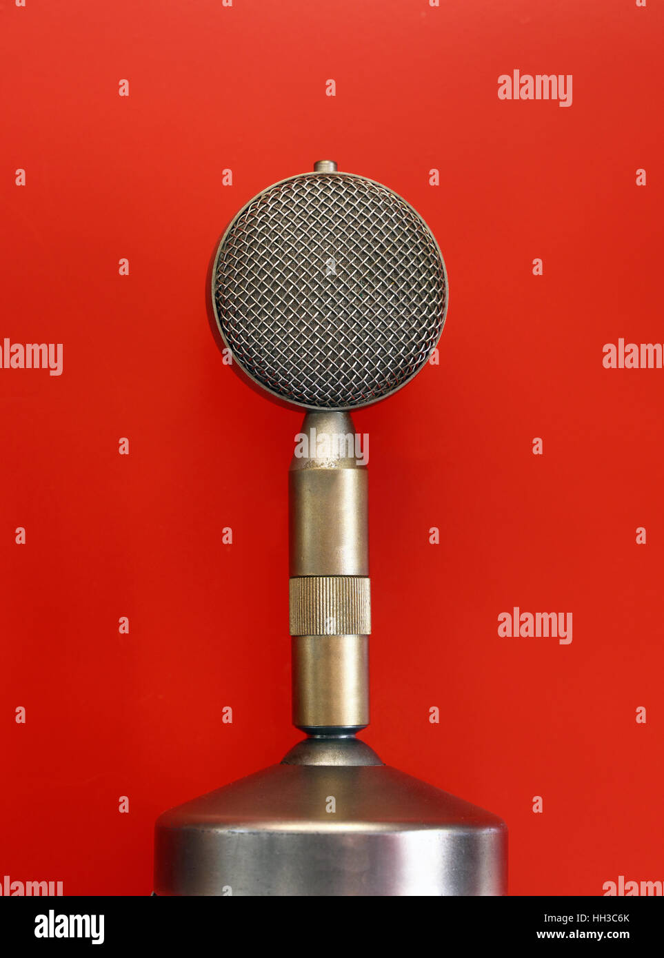 Vintage Retro antigua micrófono vocal redonda metálica vista lateral estrecha sobre fondo rojo. Foto de stock