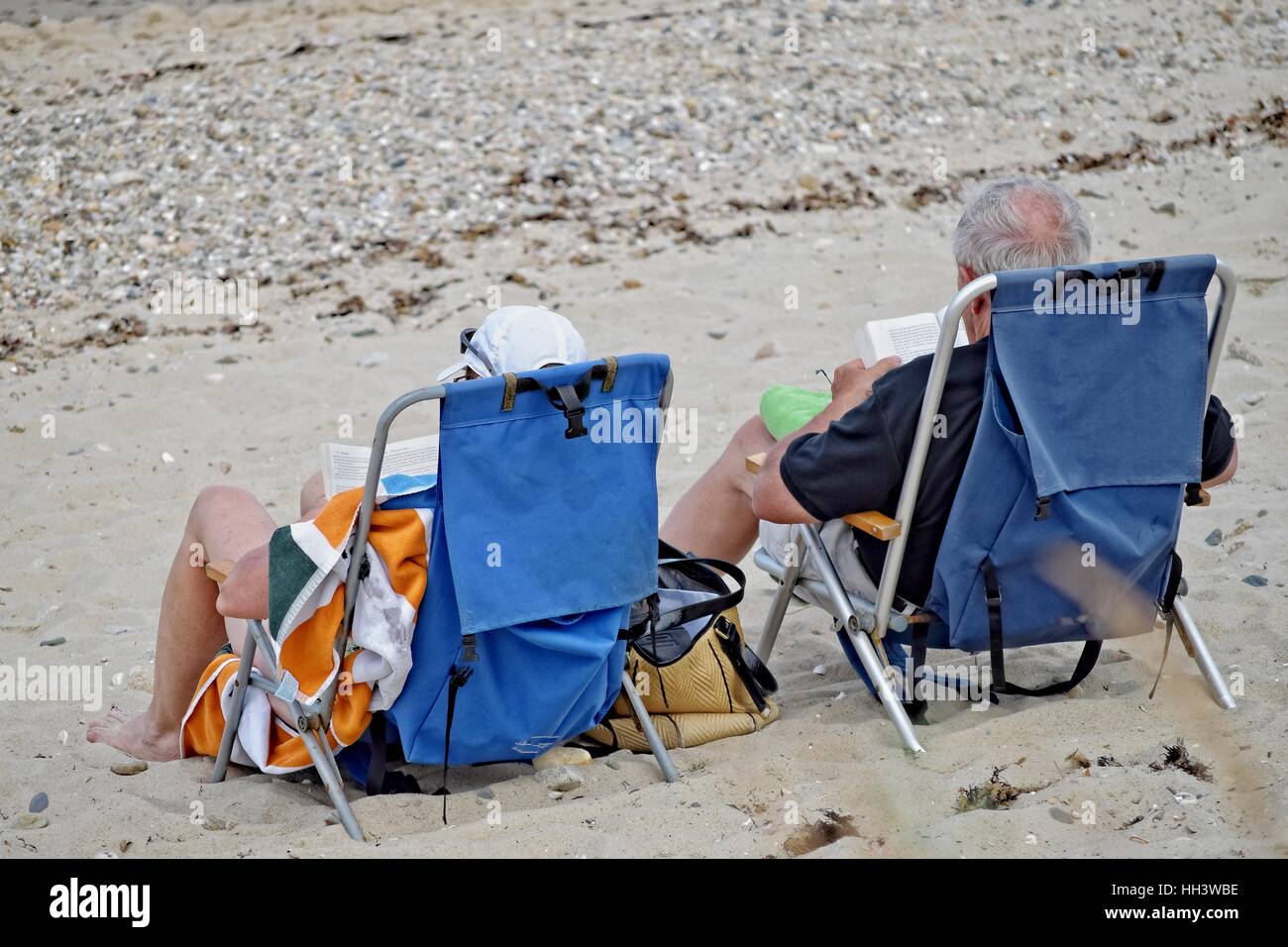 Los baby boomers leyendo en la playa con sillas de playa Foto de stock