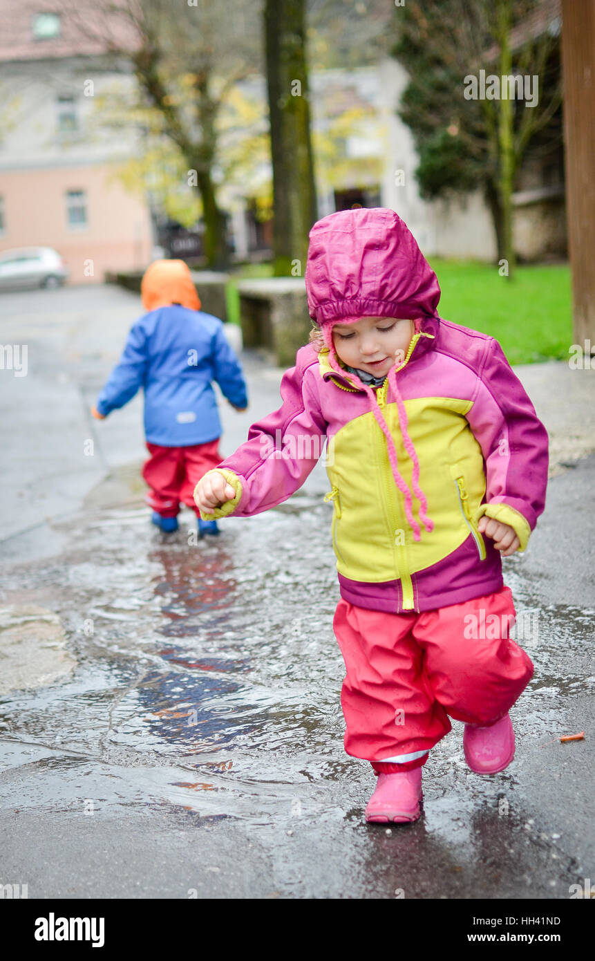 Twin bebés en ropa de lluvia, están jugando en el charco. Capa de lluvia  protección del agua - ropa impermeable Fotografía de stock - Alamy