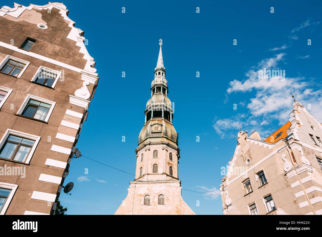 Riga, Letonia. Vista inferior de la Fleche con el reloj de la Iglesia de San Pedro, antigua torre alta, famoso entre dos edificios antiguos, cielo azul con W Foto de stock