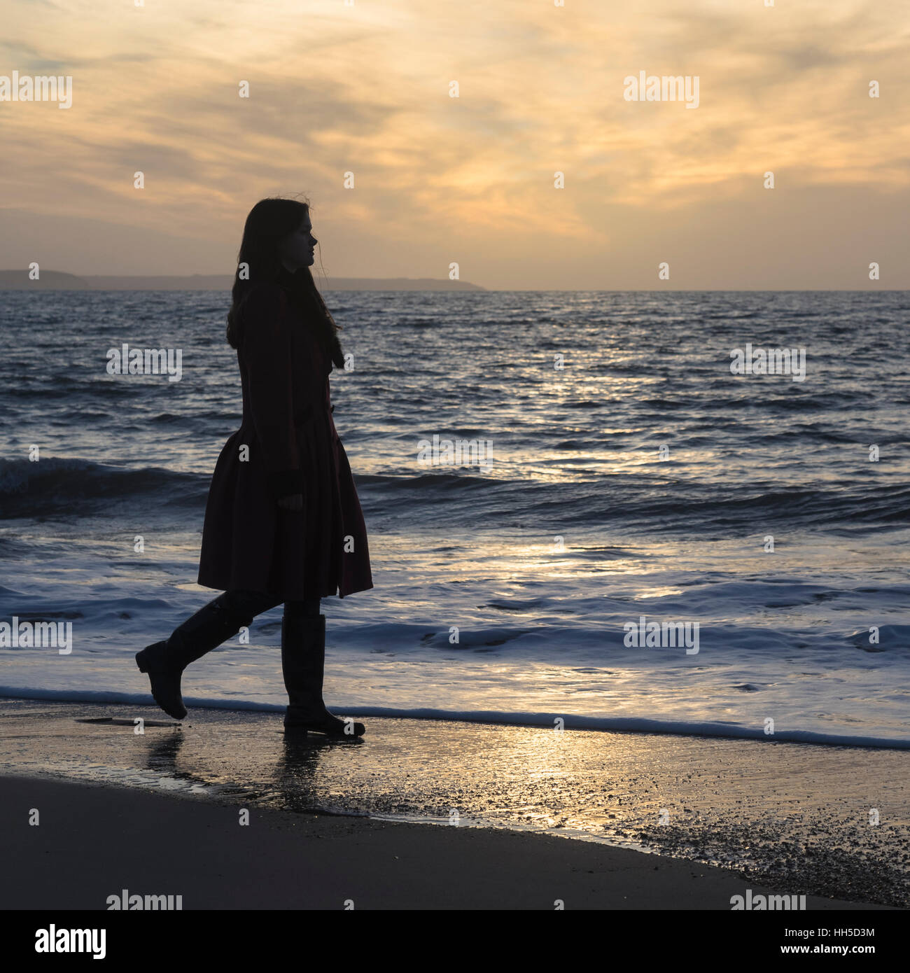Una mujer está caminando por la playa al atardecer. Foto de stock