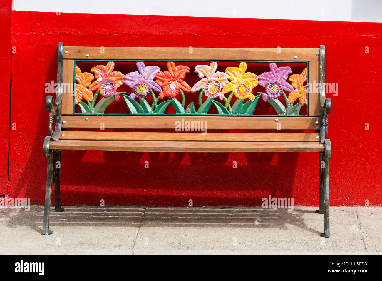 Banco con coloridos motivos florales contra una pared roja, El Jardín Colombia Foto de stock