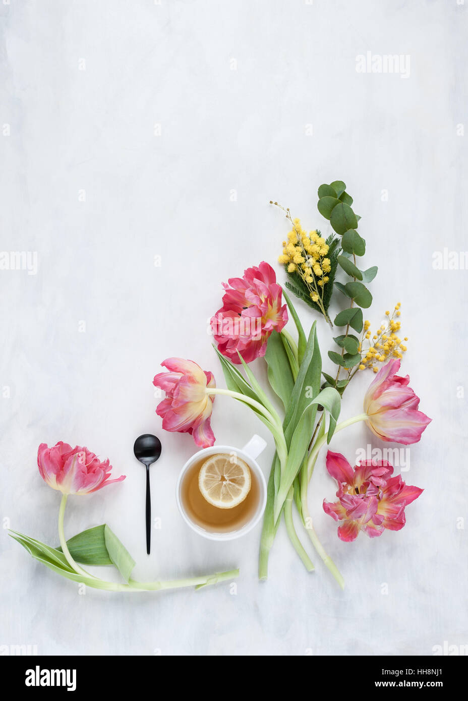 Sentar planas con tulipanes y vaso de agua establecidos en gris y blanco telón pintado con luz natural Foto de stock