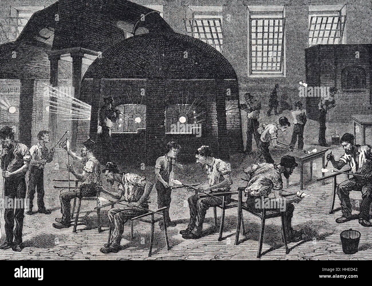 Vista general de una vidriería, mostrando los hombres participan en las  diversas etapas de hacer vasos para beber. En el fondo, a la derecha, un  hombre está utilizando un molde para soplar