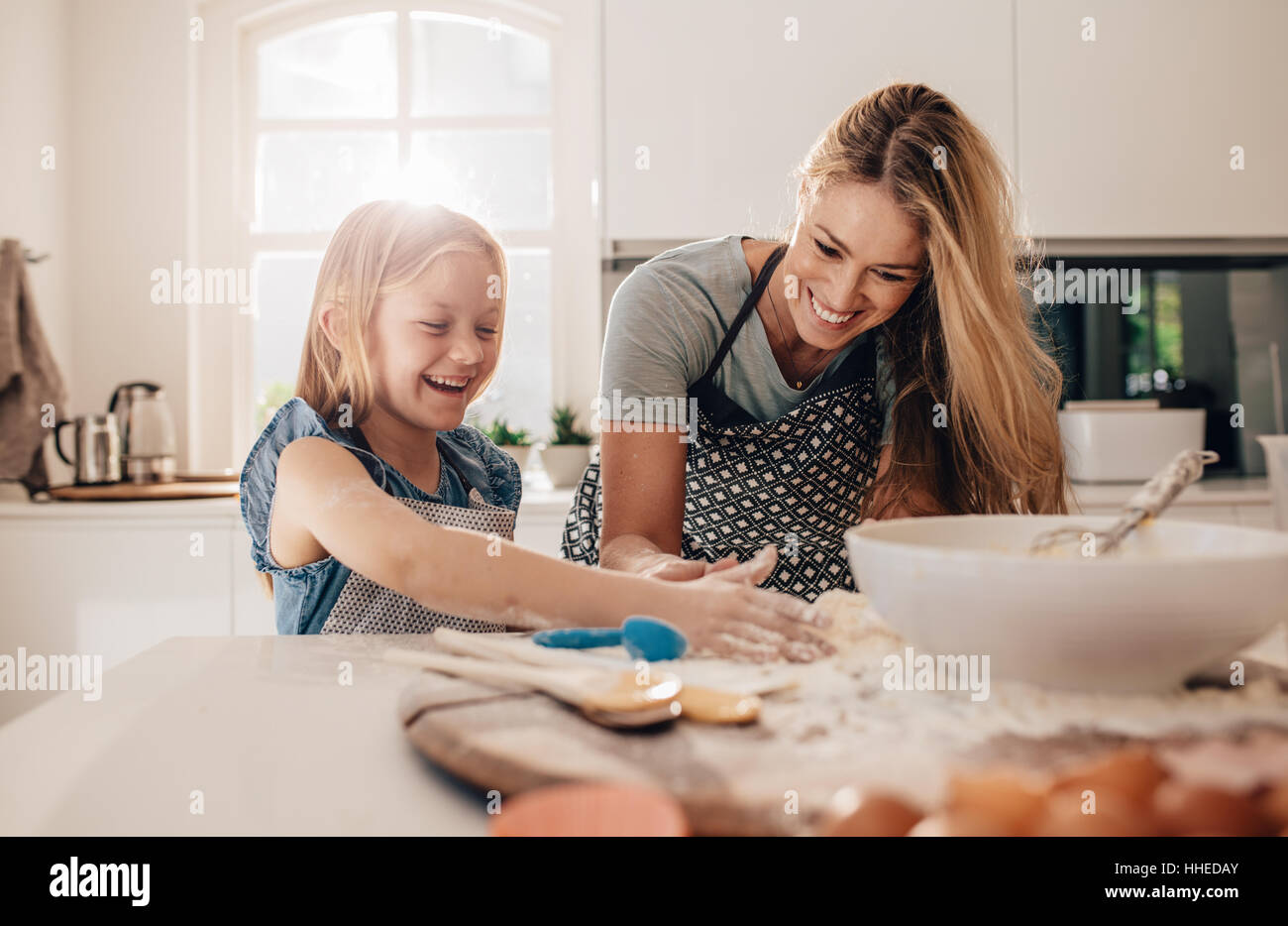 Niña feliz con su madre haciendo masa. Madre e hija en la cocina para hornear. Foto de stock