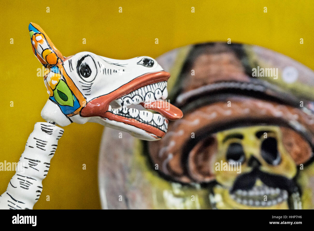 Tienda de artesanía cerámica pantalla figura de caballo con lengüeta roja colgando y placa de fondo en la pared cercana con el Día de Muertos cráneo del campesino con bigotes Foto de stock