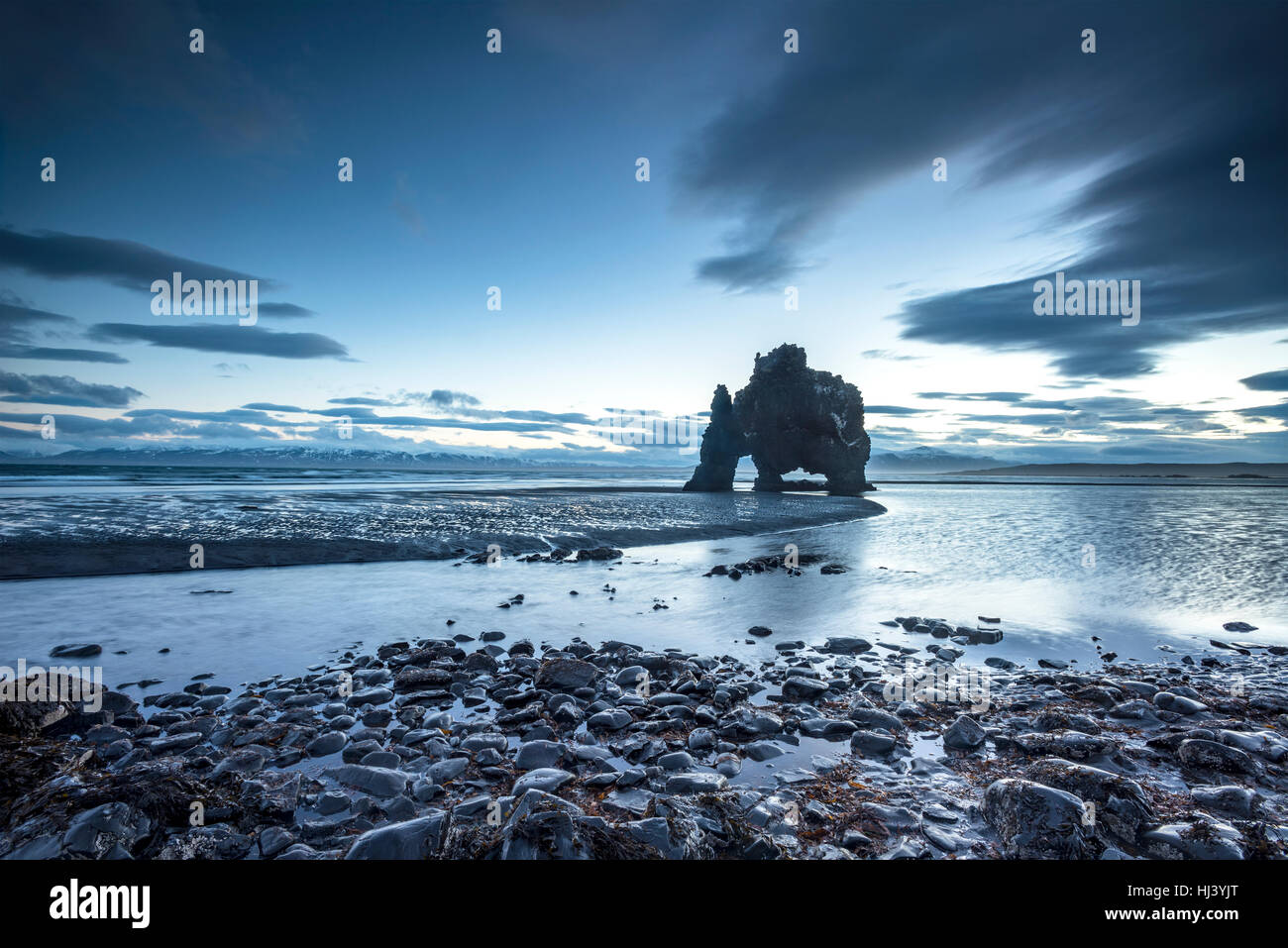 Un hito de playa en Islandia llamado dinosaurio Rock sobresale 50 pies fuera de las aguas superficiales durante un amanecer temprano. Foto de stock