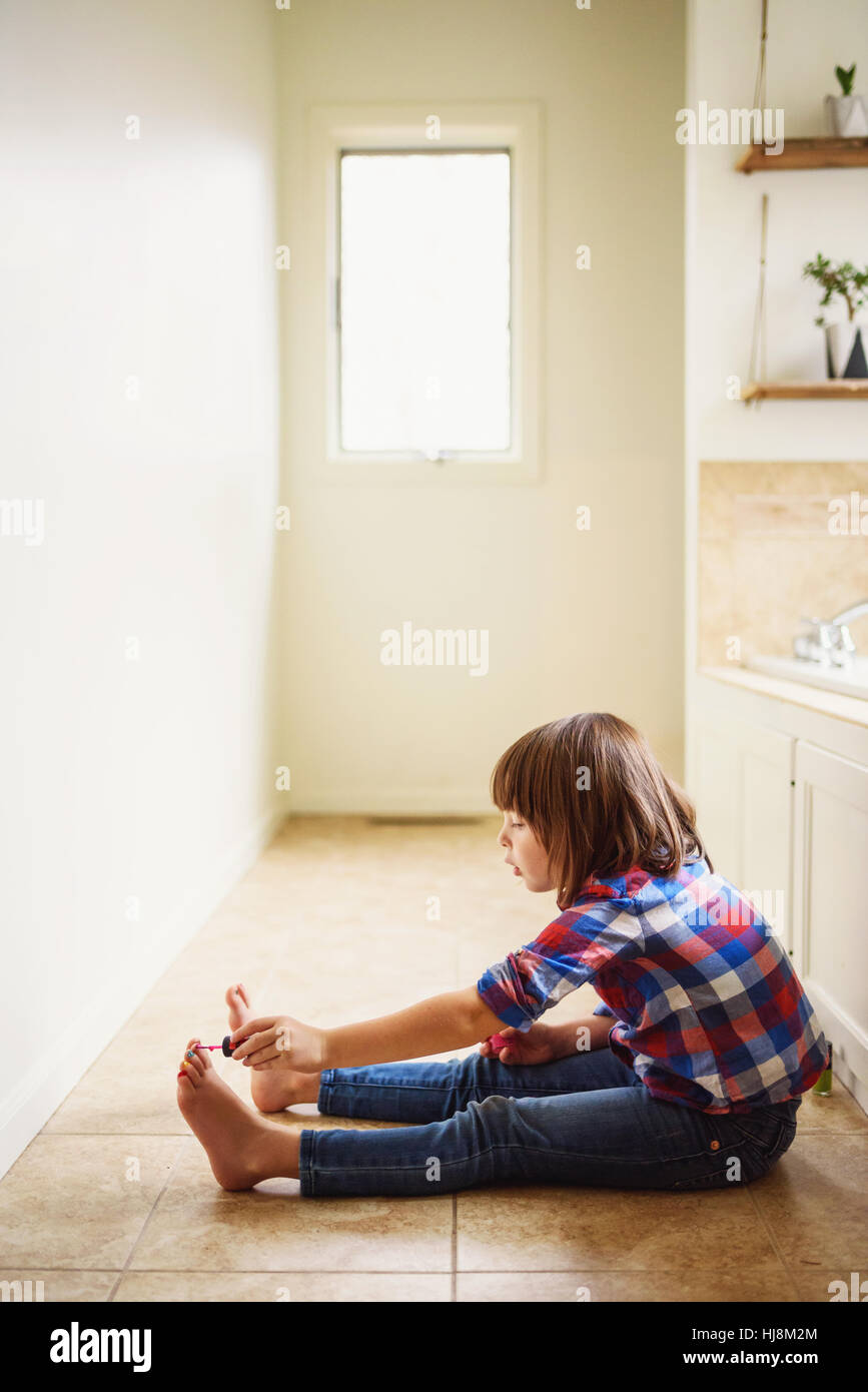 Niña sentada en el piso pintando sus uñas con laca de uñas Foto de stock