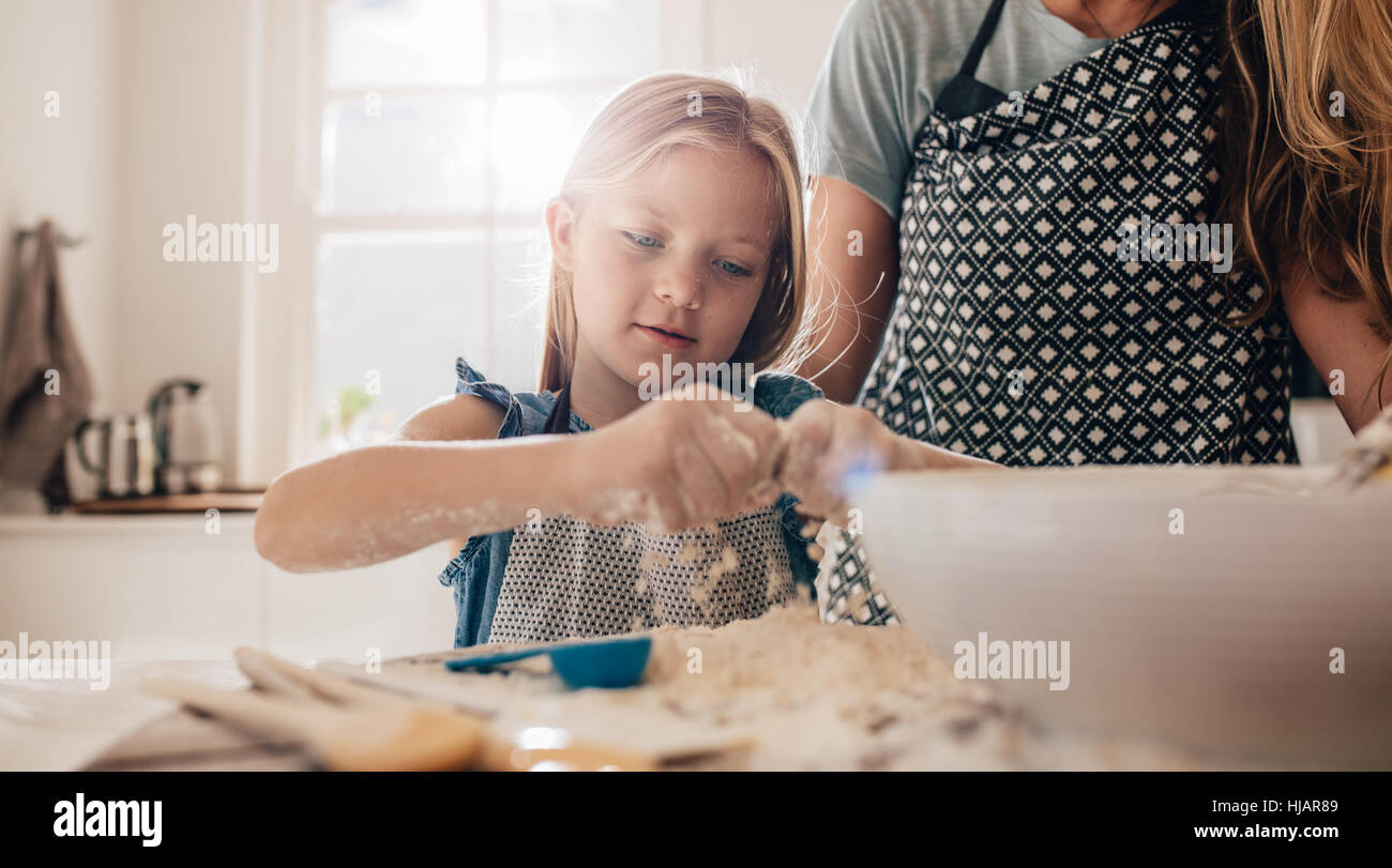 Cute Little Girl preparando la masa en la cocina con su madre. Joven aprende a cocinar. Foto de stock