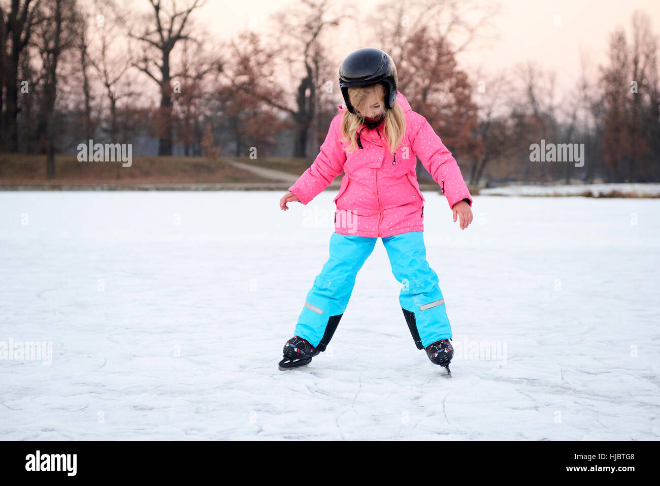 Poco feliz chica patinando en invierno afuera, vistiendo un casco de seguridad Foto de stock