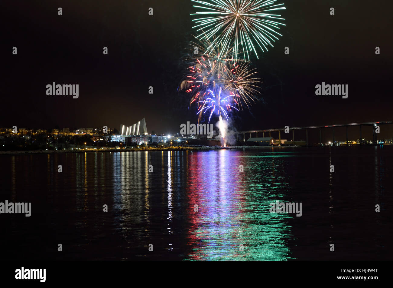 Hermosos fuegos artificiales en el cielo nocturno de la ciudad de tromsoe con puente, catedral y colorido reflejo en el fiordo de superficie de agua fría Foto de stock