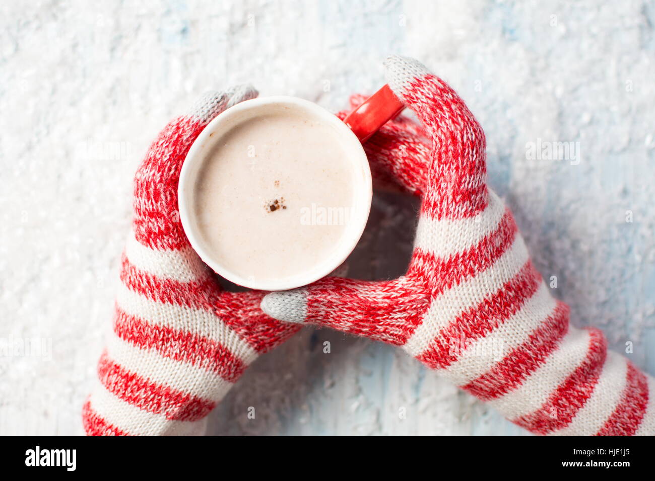 Manos femeninas en guantes celebración chocolate caliente sobre un fondo nevado Foto de stock