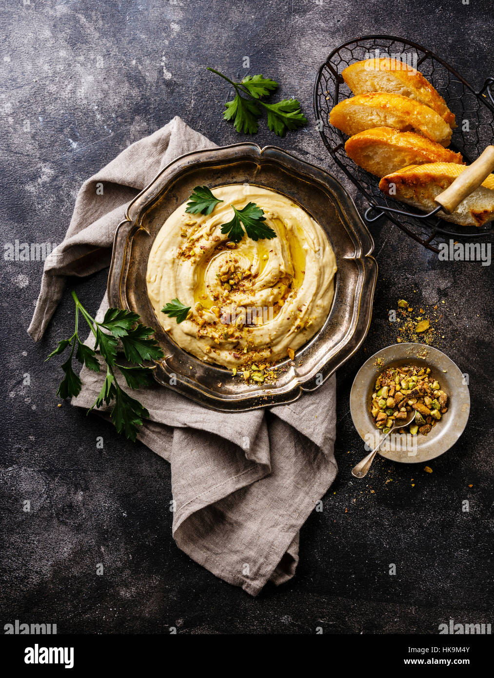Hummus casero con los pistachos y las tostadas de pan en la placa metálica negra sobre fondo de piedra Foto de stock