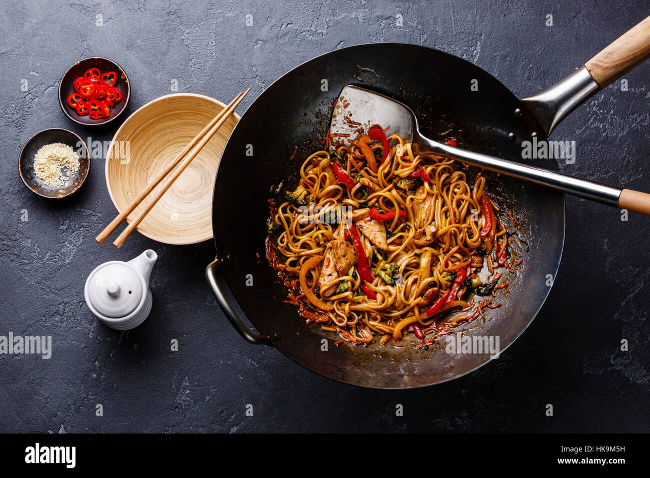 Stir-fry fideos udon con pollo y verduras en wok pan sobre fondo de piedra oscura Foto de stock