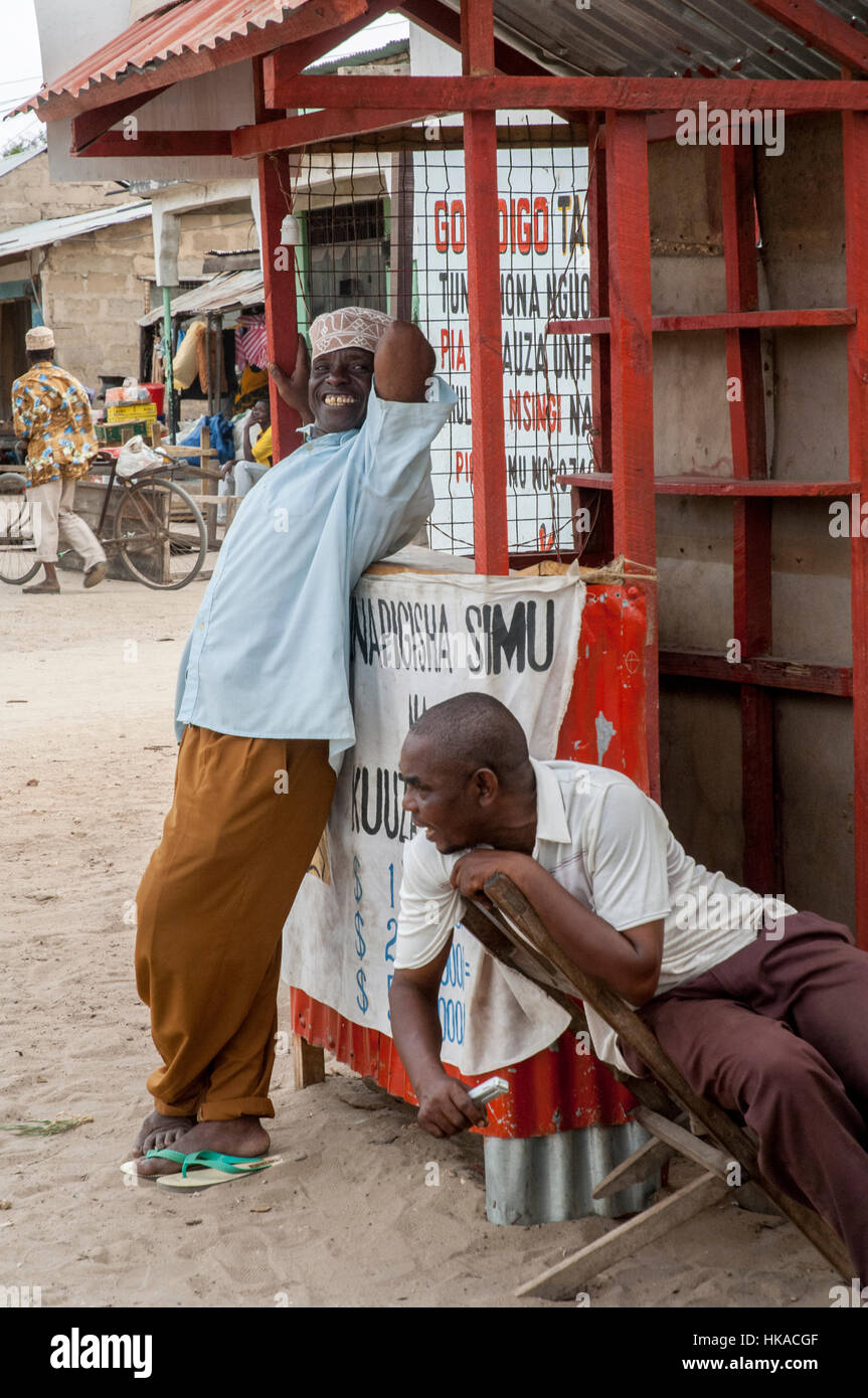Dos hombres esperando clientes delante de su kiosco vende tiempo aire para teléfonos móviles, Kilwa, Tanzania Foto de stock
