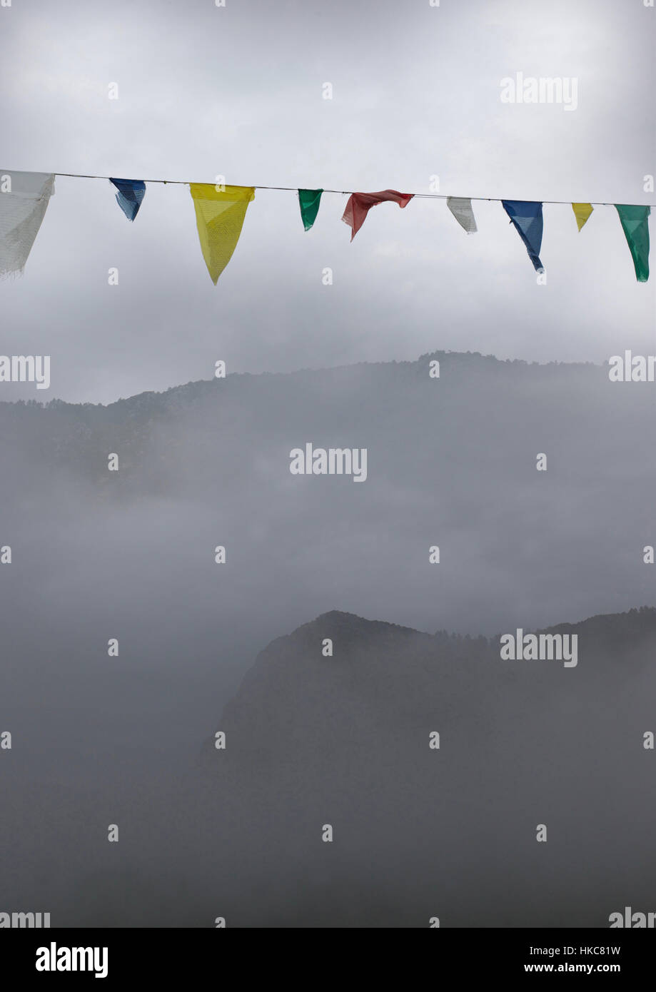Coloridas banderas de oración budista contra Un nublado cielo gris con montañas brumosas. nyma dzong en el sur de Francia Foto de stock
