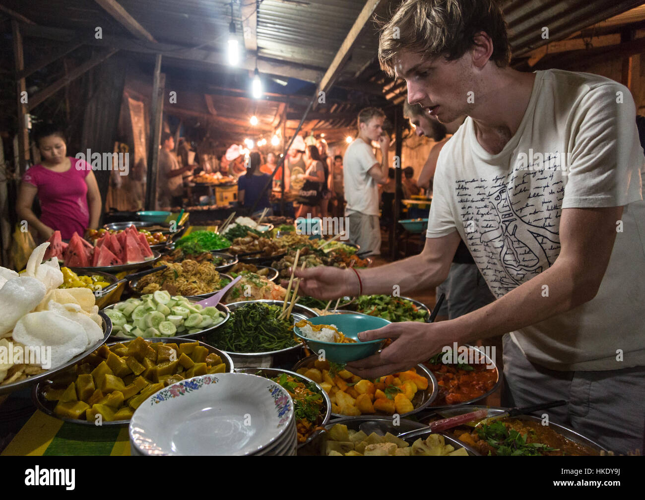 En Luang Prabang, Laos - 15 de mayo de 2015: Un joven caucásico turista compra alimentos desde un puesto en el mercado en el mercado nocturno de Luang Prabang. Foto de stock