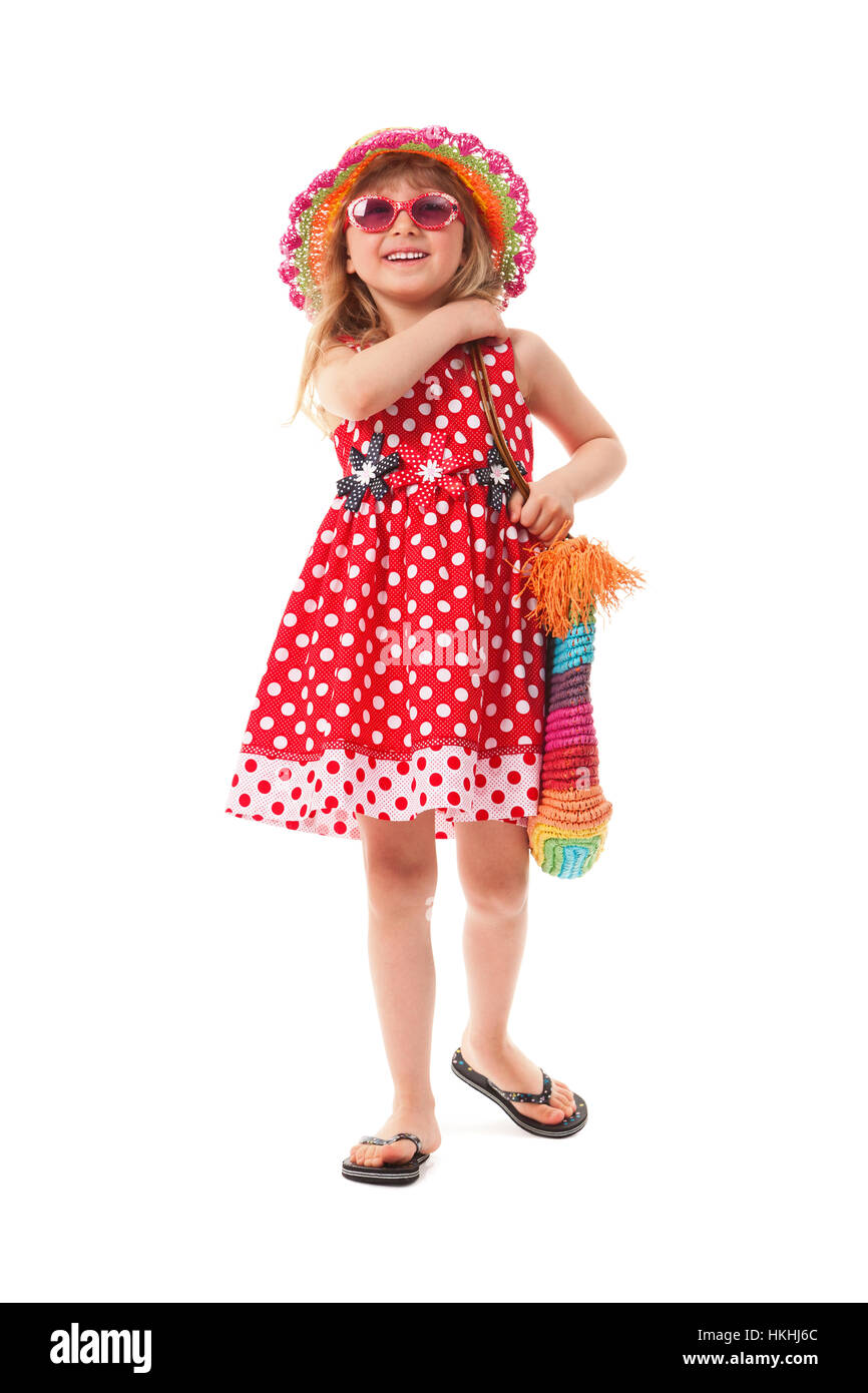 Niña vestida de rojo vestido, calzado de playa, gafas de sol y sombrero.  Ella está teniendo un brillante bolsa de playa. Ella va a ir a la playa  Fotografía de stock -