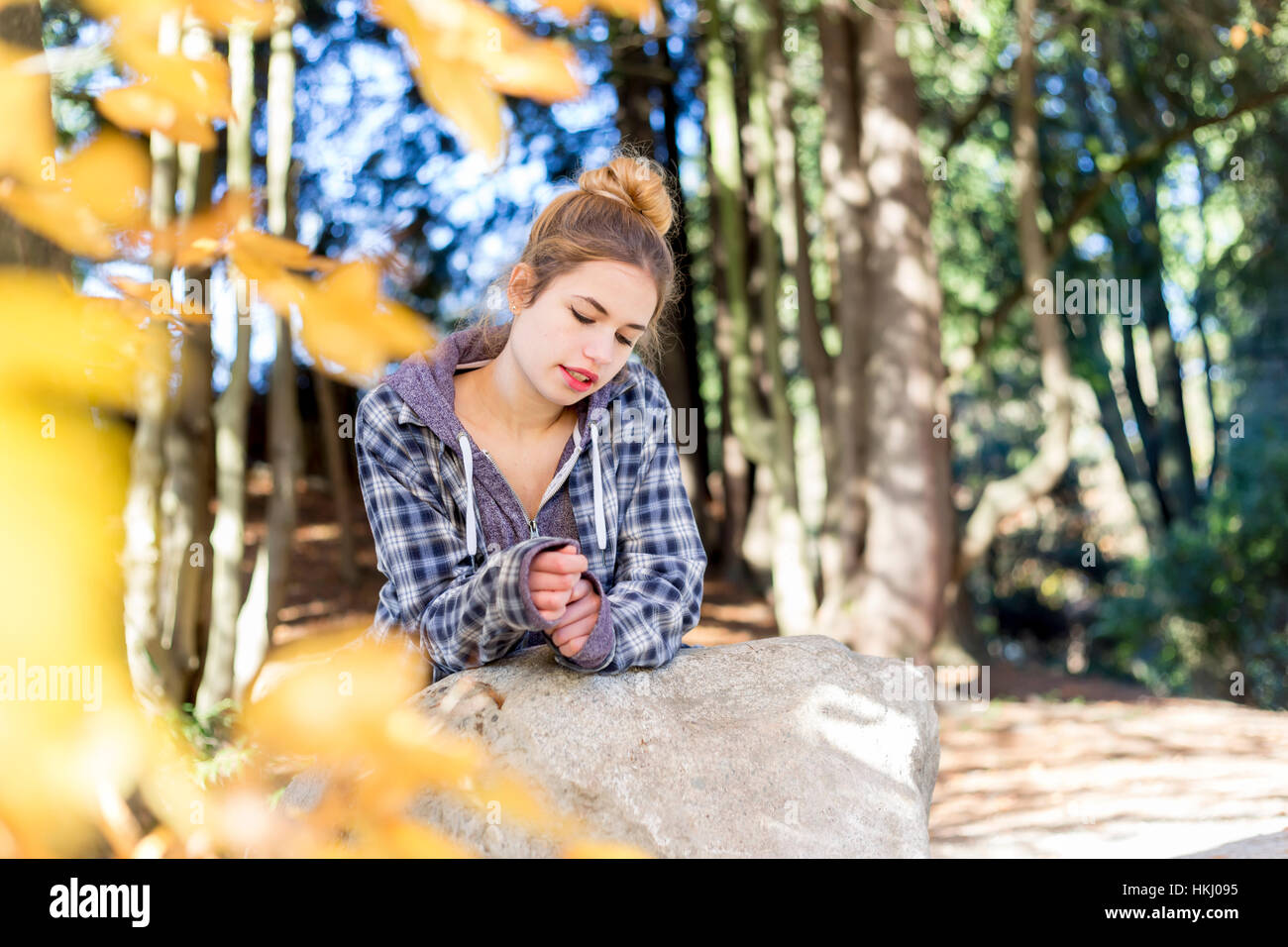 Este joven adolescente cuelga fuera solo en un parque, sentado sobre una roca en una posición desacoplada del pensamiento reflexivo para ella Foto de stock