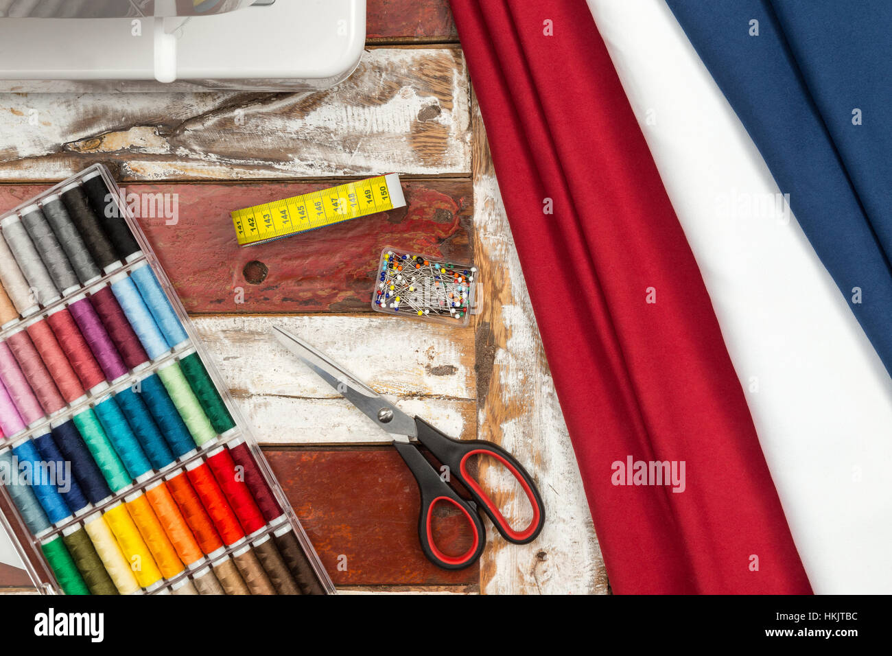Máquina de coser tijeras tela rojo blanco azul Caja con coloridos algodones cinta métrica y patilla agujas sobre mesa de madera rústica Foto de stock
