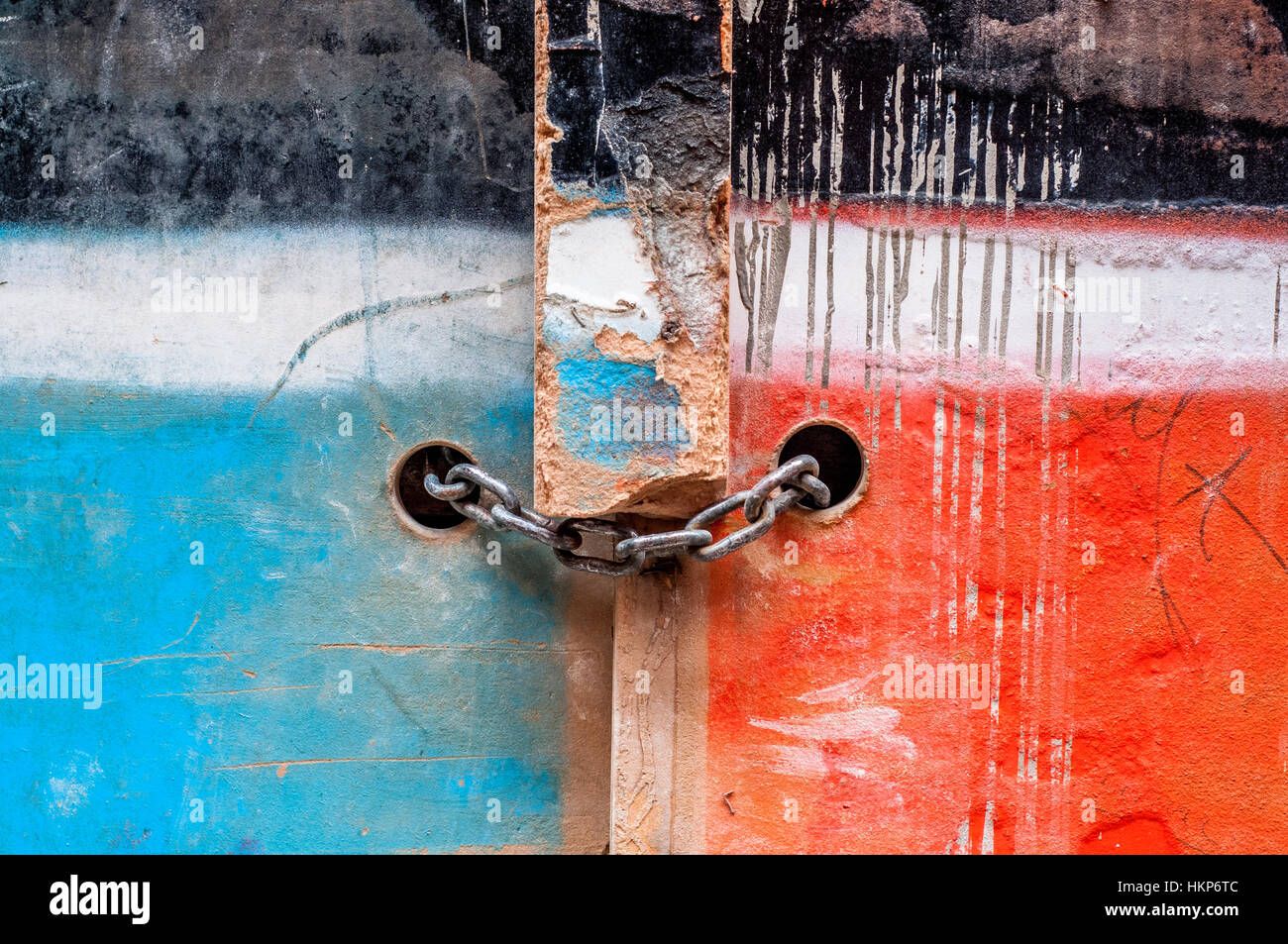 Cadena con candado en una antigua puerta de madera pintada de dos colores, azul y rojo Foto de stock