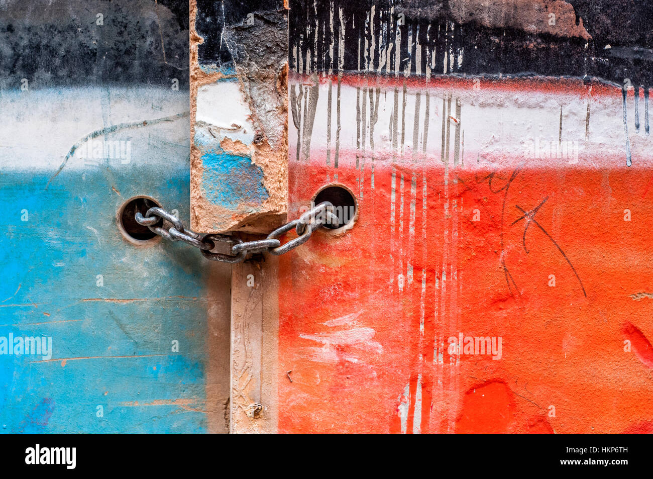 Cadena con candado en una antigua puerta de madera pintada de dos colores, azul y rojo Foto de stock
