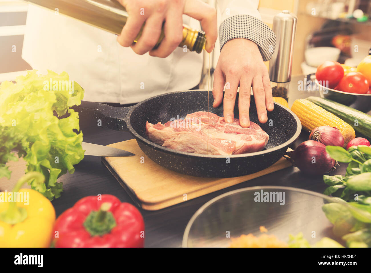 Chef vertiendo aceite sobre la carne cruda en una sartén Foto de stock