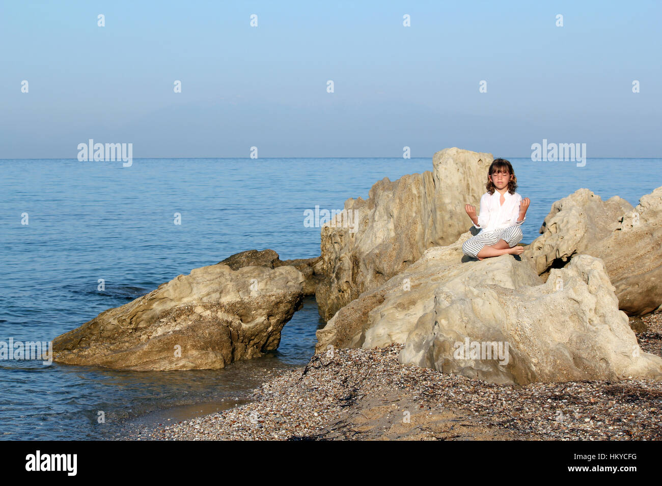 Niña sentada sobre una roca en el mar y meditar Foto de stock