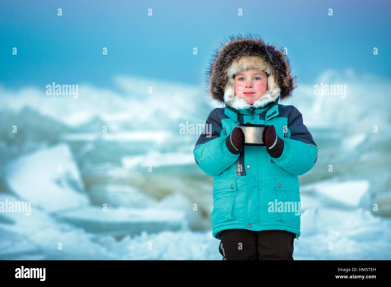 Cinco años muchacho lindo bebiendo té caliente en invierno mar congelado Foto de stock