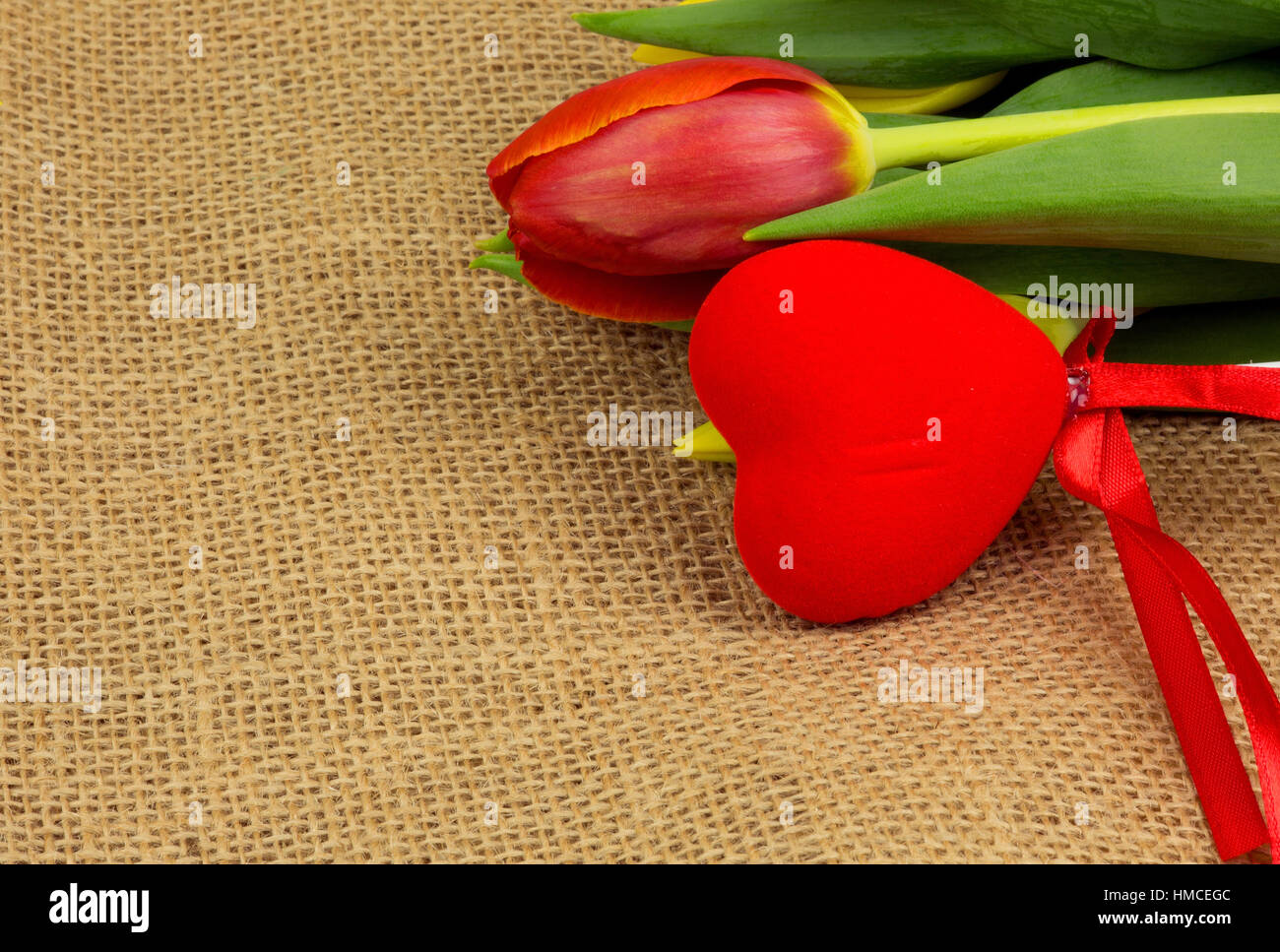 Tulipanes rojos y corazón rojo sobre un mantel bob estilo vintage. Decoración romántica de San Valentín. Vista horizontal. Foto de stock