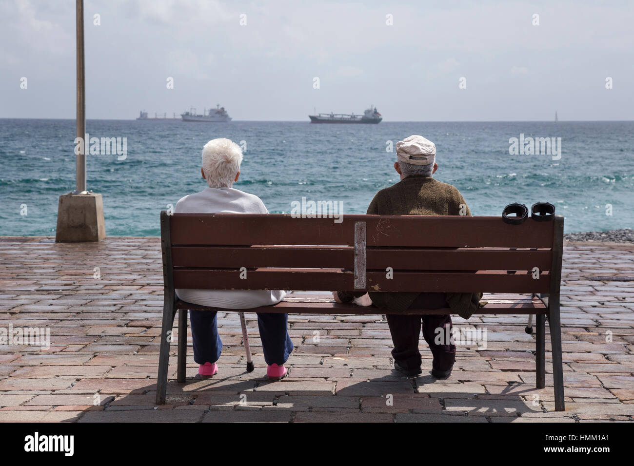 Pareja de ancianos sentados en un banco mirando los barcos en el océano, en San Cristóbal, Gran Canaria (Islas Canarias), España Foto de stock