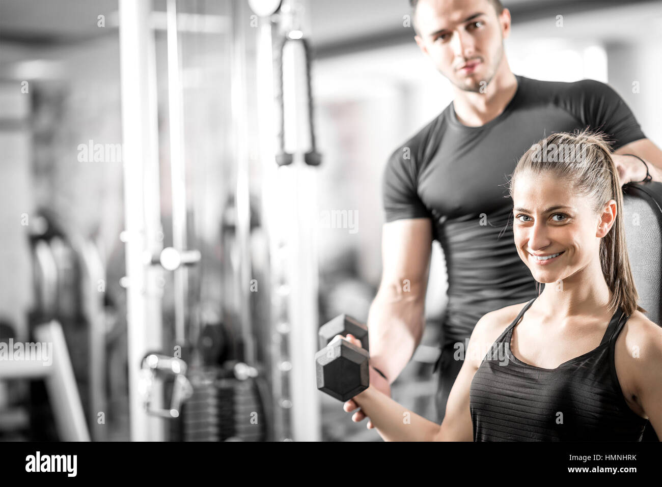 Adulto joven mujer trabajando en el gimnasio, haciendo flexiones de brazos (bíceps) con la ayuda de su entrenador personal. Foto de stock