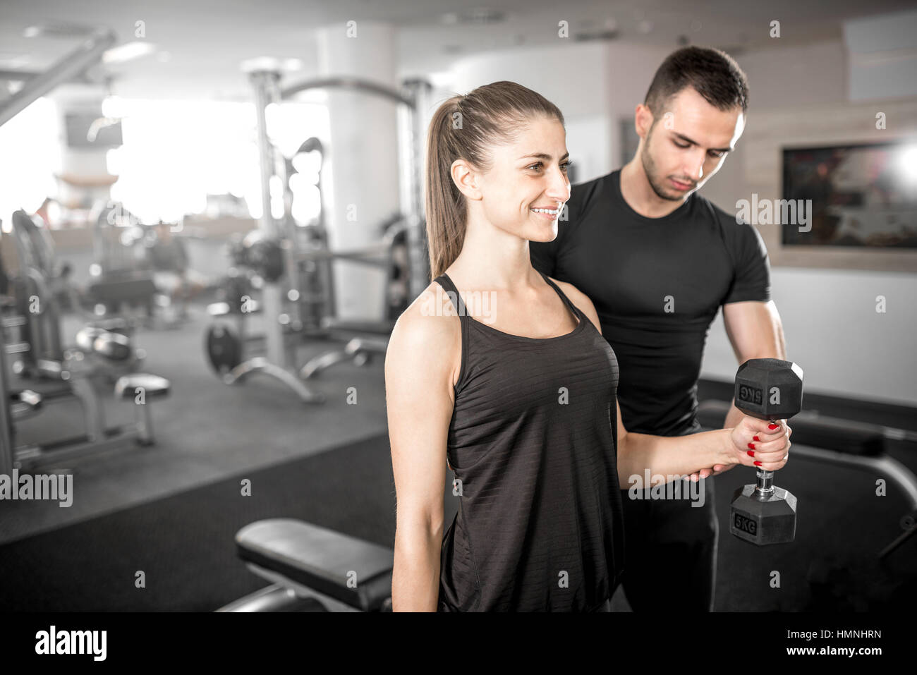 Adulto joven mujer trabajando en el gimnasio, haciendo flexiones de brazos (bíceps) con la ayuda de su entrenador personal. Foto de stock