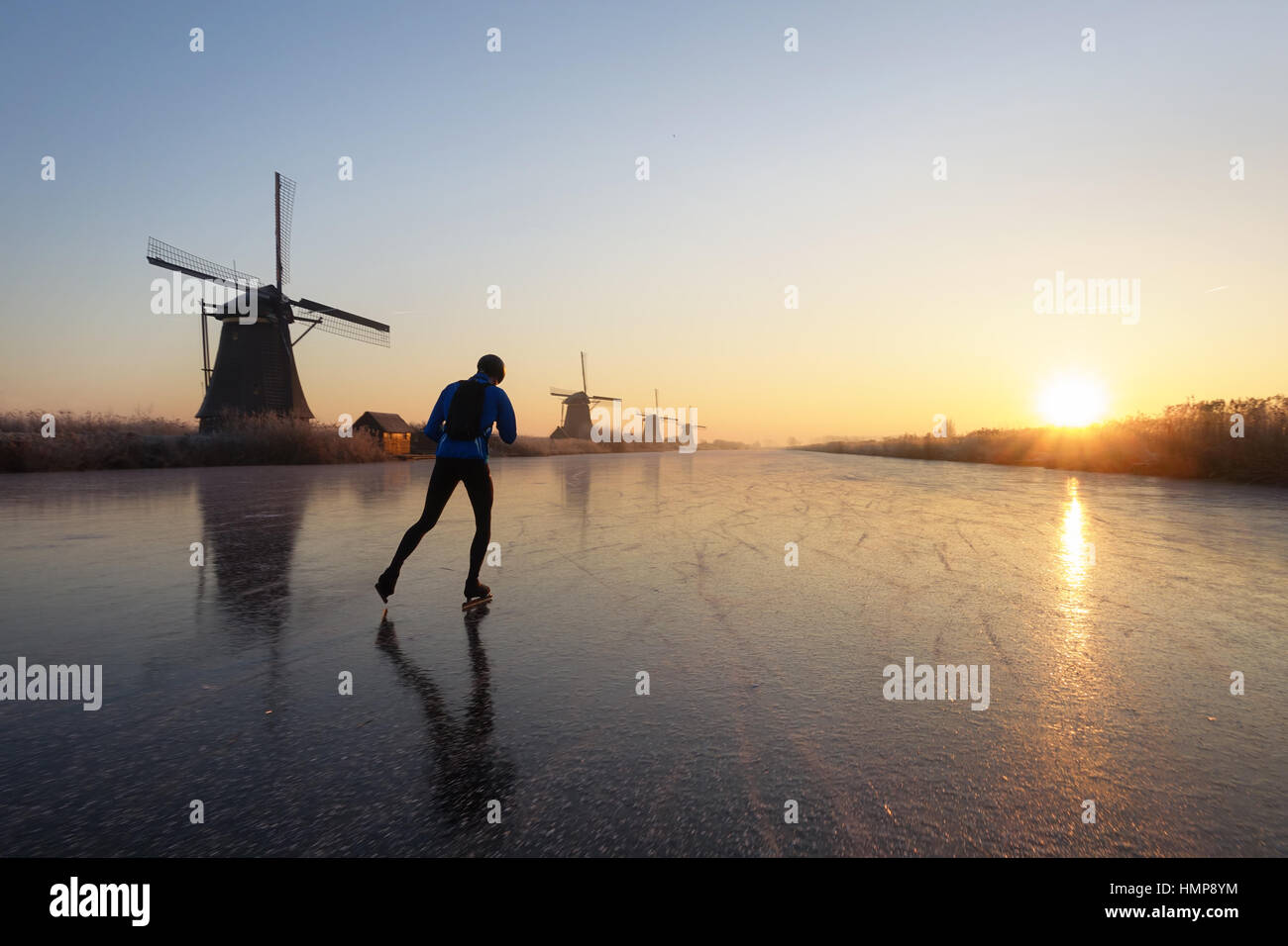 Persona solitaria del patinaje sobre hielo pasado varios molinos en el río congelado al amanecer en la mañana en Kinderdijk, Holanda en el invierno holandés. Foto de stock