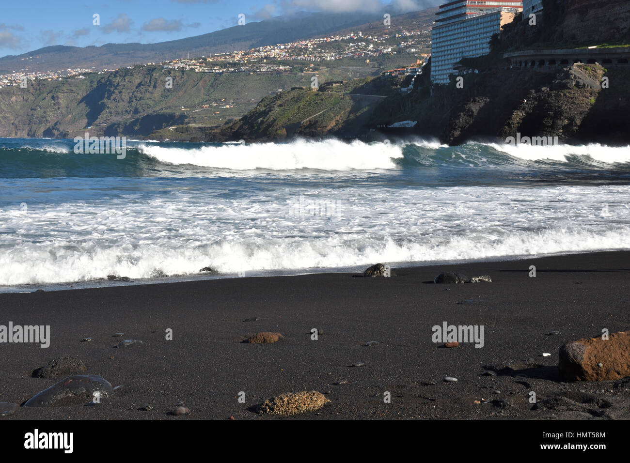 Olas contra la playa con el hotel en el fondo y la playa de arena de lava  en primer plano, imagen desde el Puerto de la Cruz Tenerife Fotografía de  stock -