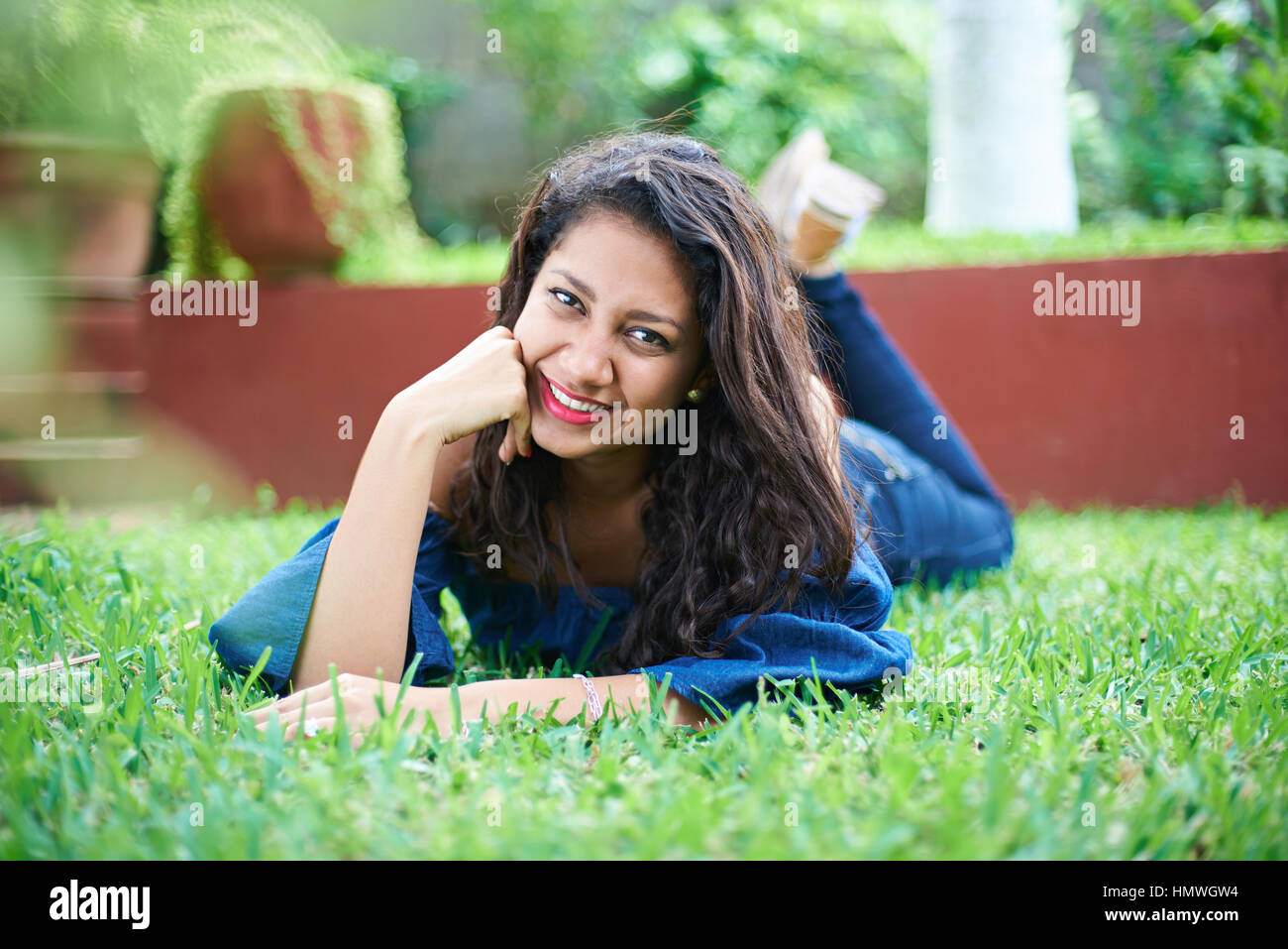 Sonriente joven latina chica recostada sobre la hierba verde Foto de stock