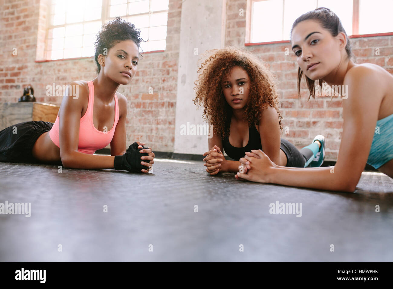 Retrato de tres jóvenes mujeres acostado en el piso del gimnasio y mirando a la cámara. Las hembras en clase de gimnasia. Foto de stock