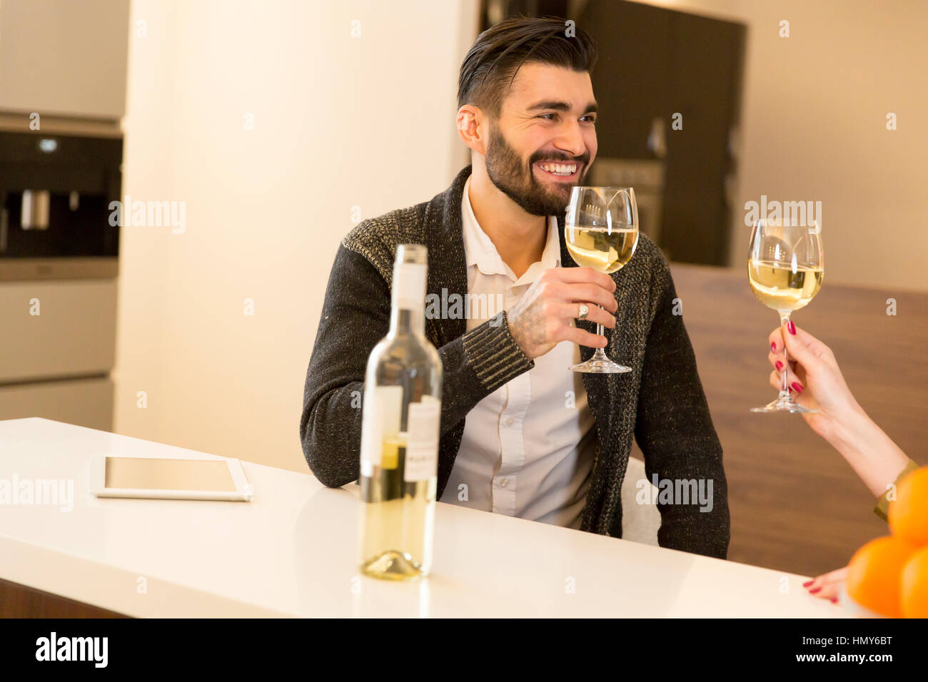 Feliz pareja brindando con vino blanco en la cocina moderna Fotografía