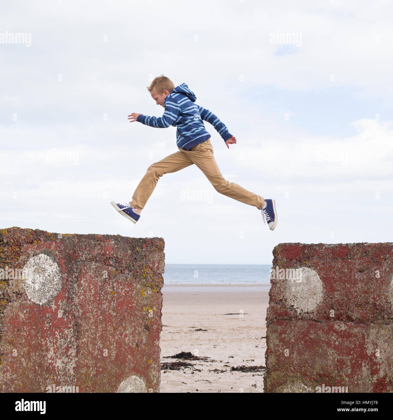 Energetic adolescente saltar de una roca a otra con la playa en el fondo. Foto de stock