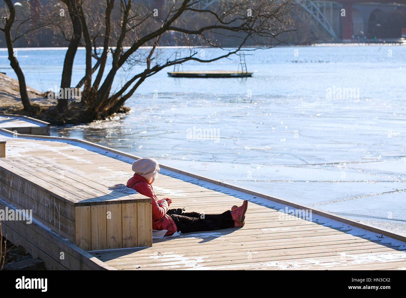 Mujer sentada sobre un embarcadero disfrutando del sol de invierno. Foto de stock