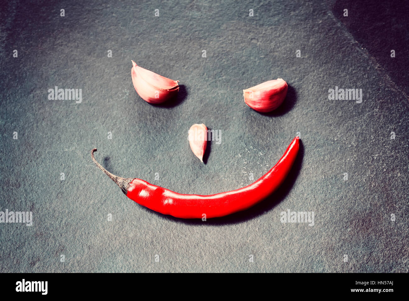 Cara sonriente de pimiento rojo y los dientes de ajo sobre fondo de pizarra, imagen conceptual, el enfoque selectivo. Foto de stock
