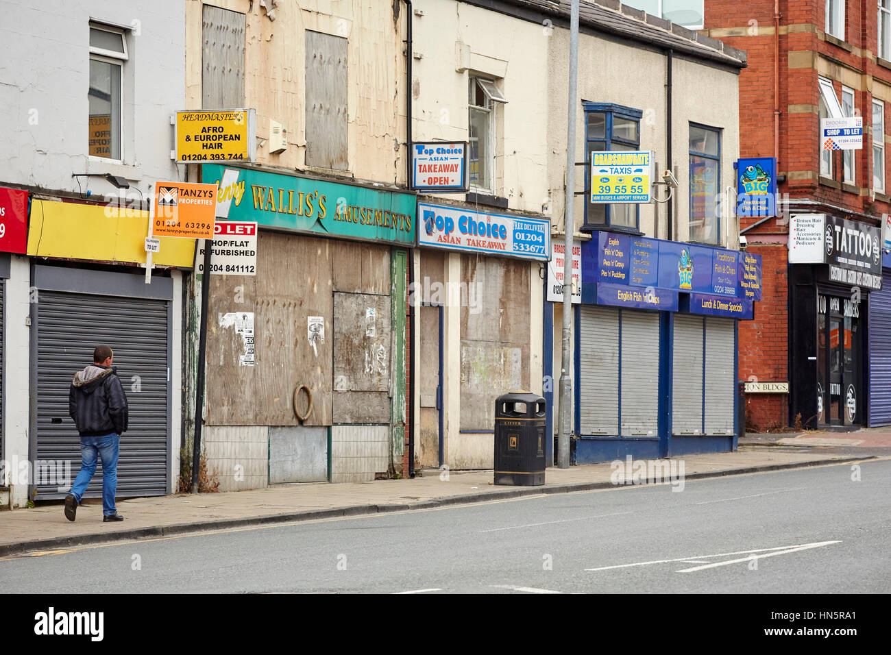 Una desacumulación cerradas y precintadas windows de minoristas independientes en una calle de casas adosadas en el centro de la ciudad de Bolton, Lancashire, Inglaterra, Reino Unido. Foto de stock