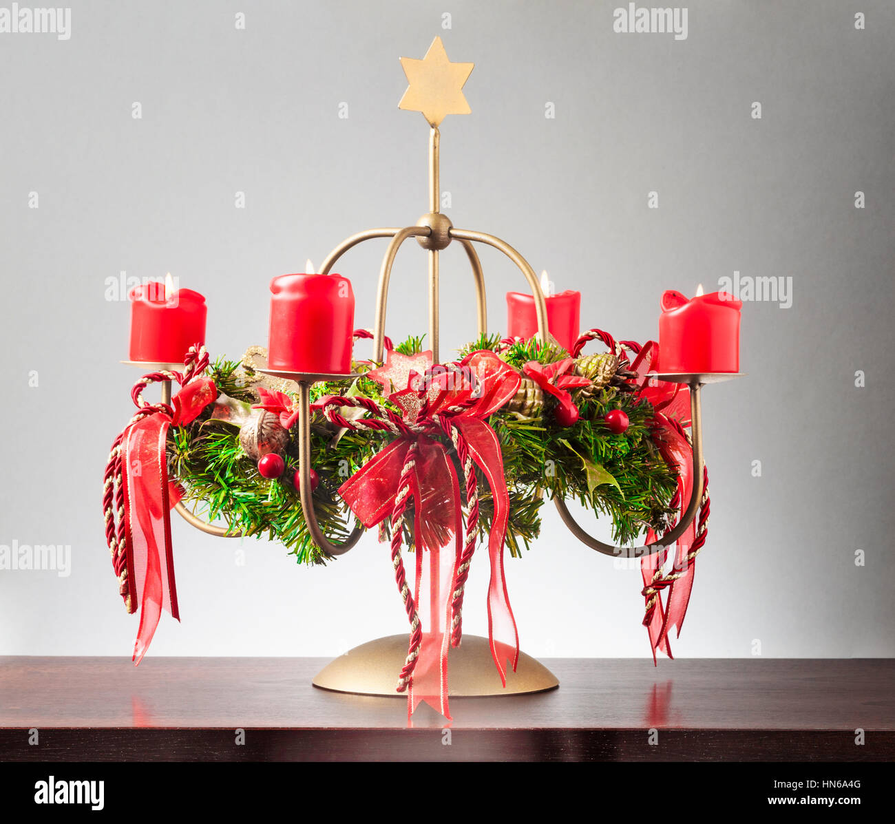 Vintage corona de adviento con cuatro velas rojas ardiente y estrella de oro sobre fondo gris, luces y decoraciones para navidad Foto de stock