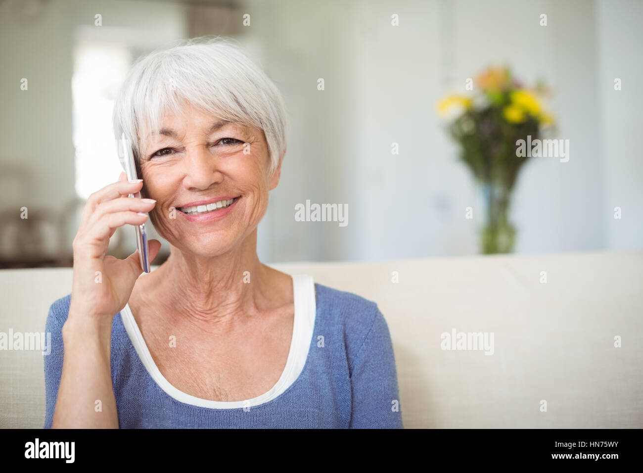 Senior sonriente mujer hablando por un teléfono móvil en el salón en casa Foto de stock